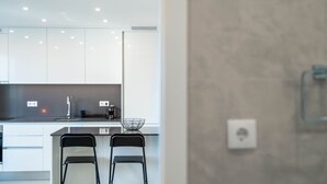 A modern kitchen with white cabinets, a black countertop, a coffee machine, and two black chairs. - Gaia Retreat by LovelyStay (Vila Nova de Gaia)