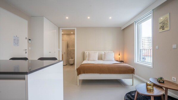 A modern bedroom with a bed, bedside table, and a window with a view of buildings.
