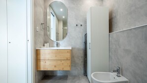A modern bathroom with a wooden vanity, a round mirror, a white sink, and a bidet. - Gaia Retreat by LovelyStay (Vila Nova de Gaia)