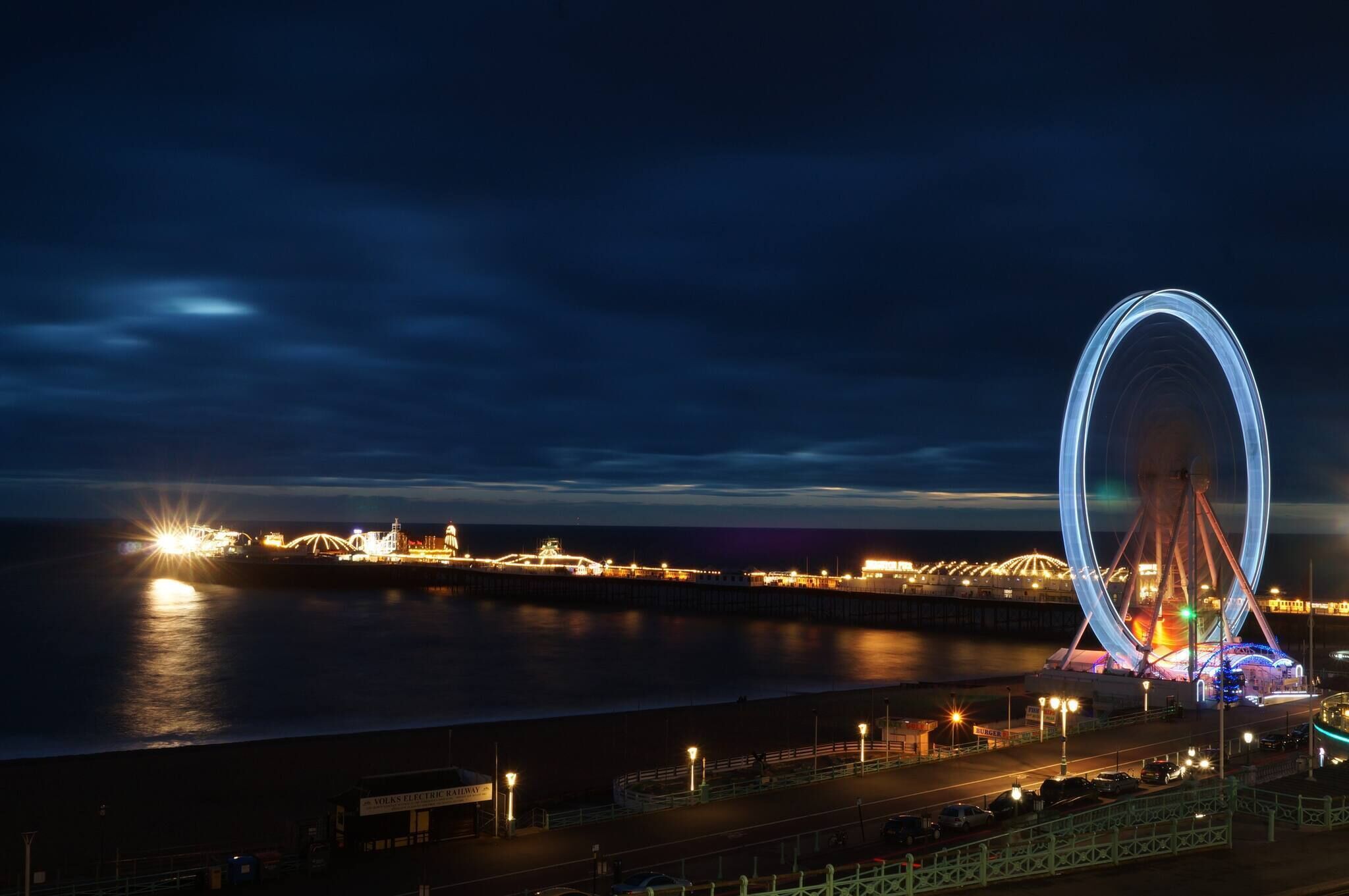Une vue sur le front de mer, avec une grande roue, une jetée illuminée et un pont en arrière-plan.