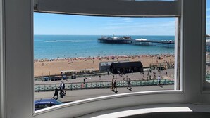 A beach view through a window, including a pier, beachgoers, and a building labeled 'Val's Electric.' - Seaview Regency Apartment With Private Parking (Brighton)