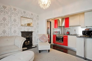 A living room with a sofa, a fireplace, and a kitchen with red cabinets and stainless steel appliances.