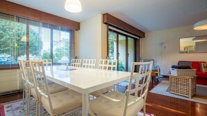 Un coin repas avec une table et des chaises blanches, un canapé rouge et une grande fenêtre avec des stores.