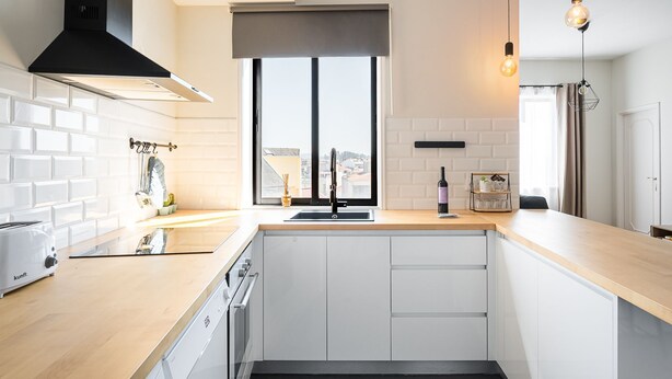 A modern kitchen with white cabinetry, a black range hood, a window with a view, and a wine bottle on the counter. - Catarina's Little Corner by LovelyStay (Porto)