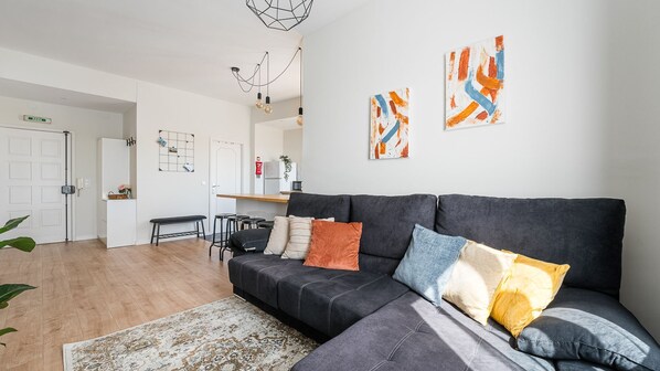 Un salon moderne avec un canapé gris, des coussins colorés, un tapis à motifs et des œuvres d’art abstraites accrochées au mur.