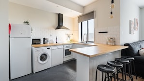 A modern kitchen with a central island, bar stools, a washing machine, a microwave, and a sink. - Catarina's Little Corner by LovelyStay (Porto)