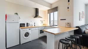 A modern kitchen with a central island, bar stools, a washing machine, a microwave, and a sink.