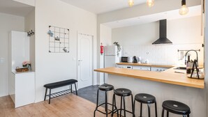 A modern kitchen with a wooden countertop, black bar stools, a white refrigerator, and a grid-patterned wall decoration. - Catarina's Little Corner by LovelyStay (Porto)