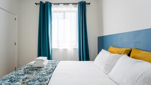 A hotel room with a bed, a window with curtains, a bedside table with towels, and a headboard with pillows. - Catarina's Little Corner by LovelyStay (Porto)