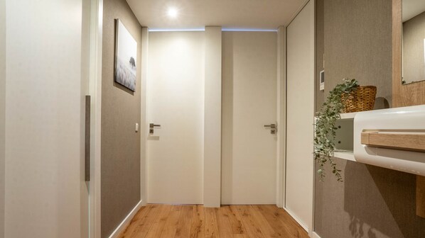 A hallway with wooden flooring, a white door, a wall-mounted picture, and a small plant on a shelf.