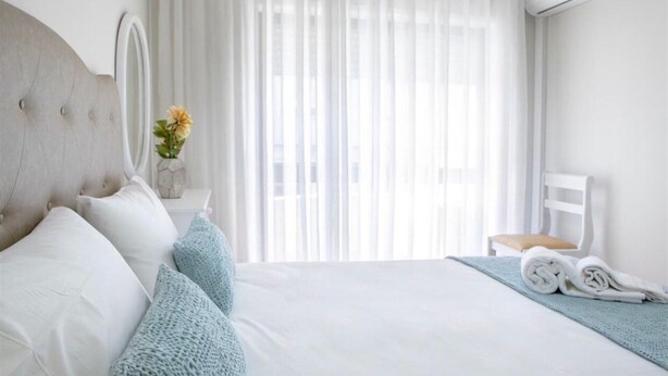 A hotel room with a large bed, a headboard, a bedside table with a vase of flowers, a chair, and a window with sheer curtains. - Belas Artes Apartment by LovelyStay (Porto)