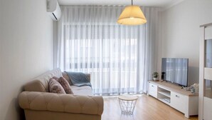 A modern living room with a sofa, a TV, and a dining table. - Belas Artes Apartment by LovelyStay (Porto)