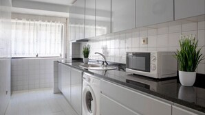A modern kitchen with white cabinetry, a built-in washing machine, a microwave, and a sink with a faucet. - Belas Artes Apartment by LovelyStay (Porto)