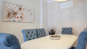 A dining area with a round table, four blue upholstered chairs, a white bowl, and a floral painting on the wall. - Belas Artes Apartment by LovelyStay (Porto)