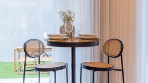 Une table ronde, deux chaises en osier, un vase avec des fleurs séchées, ainsi que des assiettes et des verres posés sur la table.