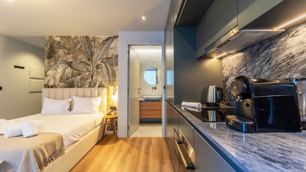 Une chambre d’hôtel moderne comprenant un lit, une salle de bain avec un miroir et un coin cuisine équipé d’une machine à café.