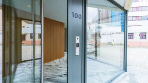 Une entrée moderne avec une porte en verre, un mur recouvert de panneaux en bois et une serrure à clavier numérique.