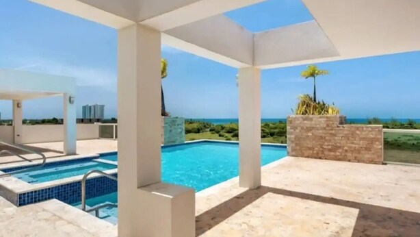 A modern outdoor pool area with a clear view of the ocean and a covered seating area.