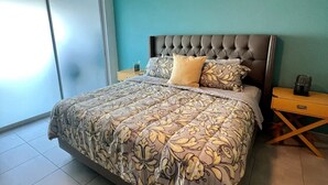 A bedroom with a large bed, a tufted headboard, a nightstand, and a sliding glass door.