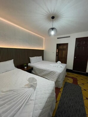 A hotel room with two beds, a small table, a potted plant, and a door.