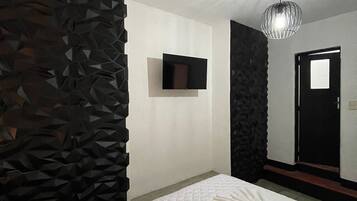 Una habitación de hotel moderna con una cama grande, un televisor de pantalla plana montado en la pared y un revestimiento texturizado único en una pared.