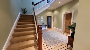 A staircase with a wooden handrail and beige carpeted steps, leading to a landing with a patterned rug and a door. - Victorian stone mansion in extensive grounds overlooking Bala Lake (Bala)