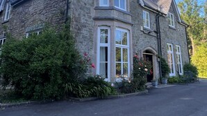 A stone building with a bay window, a chimney, and a door with a small porch. - Victorian stone mansion in extensive grounds overlooking Bala Lake (Bala)