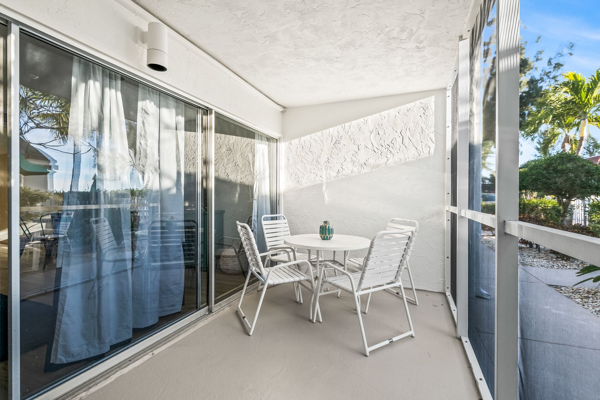 A balcony with a glass door, white metal chairs, a small round table, and a decorative vase.