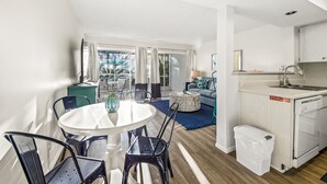 Un espace de vie compact comprenant un coin repas, une kitchenette et une vue dégagée sur l’extérieur grâce à une porte-fenêtre coulissante.