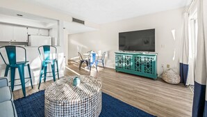 Un salon moderne avec une table basse ronde, des fauteuils de couleur turquoise, un meuble de rangement turquoise et un téléviseur à écran plat.