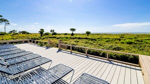 Une terrasse en bois avec des chaises longues en métal, donnant sur une pelouse agrémentée de palmiers.