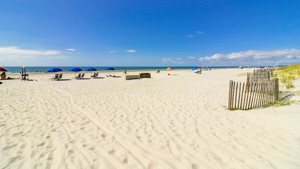 Une plage avec plusieurs chaises longues et des parasols, une clôture en bois et un ciel bleu dégagé.