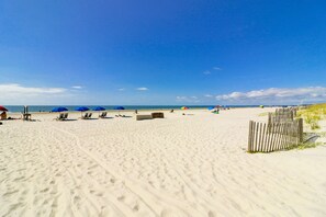 A beach with several sun loungers and umbrellas, a wooden fence, and a clear blue sky. - Sunset Rentals | Seaside 160 (Hilton Head Island)
