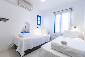 Une chambre d’hôtel avec deux lits, une fenêtre avec des rideaux bleus, une petite table avec une lampe et un climatiseur fixé au mur.