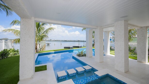 A pool area with a view of the water, surrounded by palm trees and a clear sky.