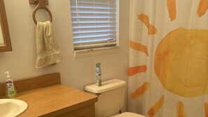 A bathroom with a wooden vanity, a toilet, a window with blinds, and a shower curtain with a sun design. - Spacious retreat on beautiful Lake June. Lake Placid, FL (Lake Placid)