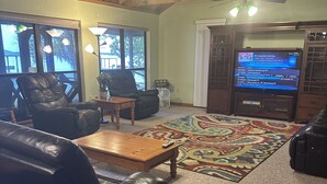 A living room with a wooden ceiling, a large TV, leather chairs, a coffee table, and a patterned rug. - Spacious retreat on beautiful Lake June. Lake Placid, FL (Lake Placid)
