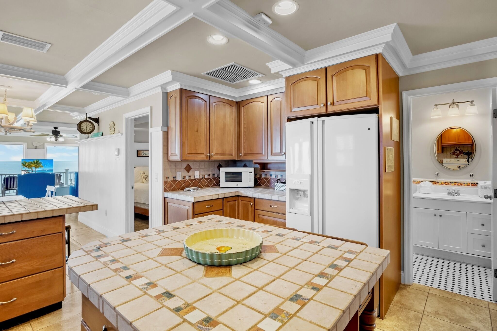 A kitchen with wooden cabinets, a white refrigerator, a microwave, and a tiled island.