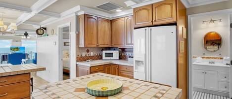 A kitchen with wooden cabinets, a white refrigerator, a microwave, and a tiled island.