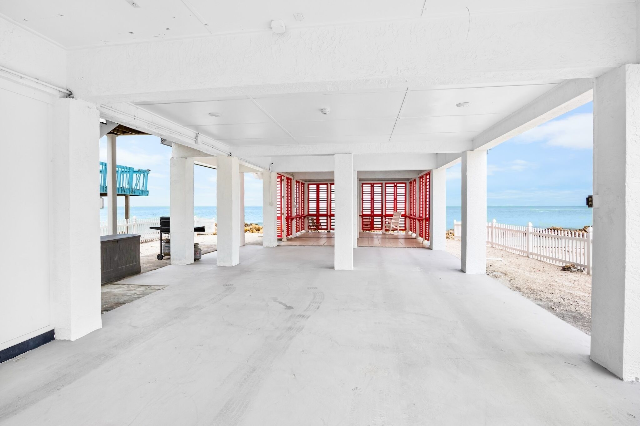 Ein großzügiger überdachter Bereich mit Blick auf den Strand, der eine weiße Decke, einen Betonboden und rote Geländer aufweist.