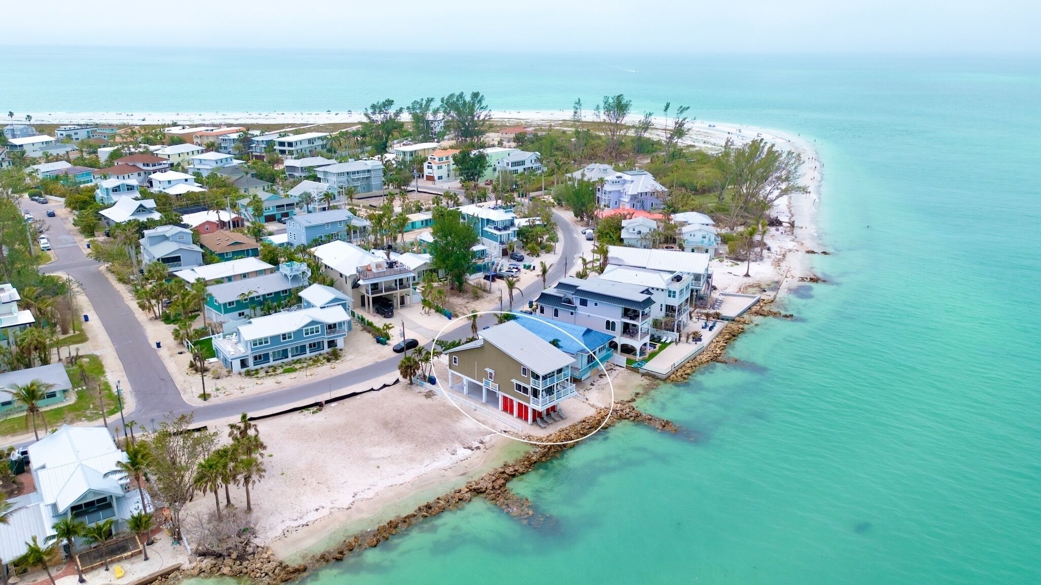 A coastal residential area with houses near a beach, featuring a road and clear turquoise waters.