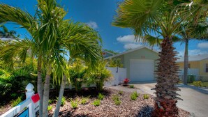 A residential property with a garage, a well-maintained garden with palm trees, and a white picket fence. - Single-Level Beach Home, Short Walk to Sand! Close to Dining, Shopping, and More (Holmes Beach)