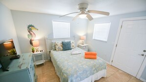 A bedroom with a bed, two bedside tables, a ceiling fan, a door, and a wall-mounted decorative piece. - Single-Level Beach Home, Short Walk to Sand! Close to Dining, Shopping, and More (Holmes Beach)