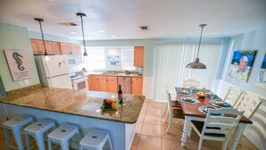A kitchen with a central island, bar stools, a dining table set with plates and glasses, and a refrigerator. - Single-Level Beach Home, Short Walk to Sand! Close to Dining, Shopping, and More (Holmes Beach)