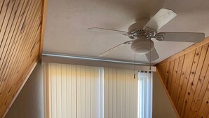 A bedroom with a sloped ceiling, a ceiling fan, a bed with a patterned bedspread, and a window with vertical blinds. - Family Retreat at Conneaut Lake, PA ideal for family fun or relaxing get- away!  (Conneaut Lake)