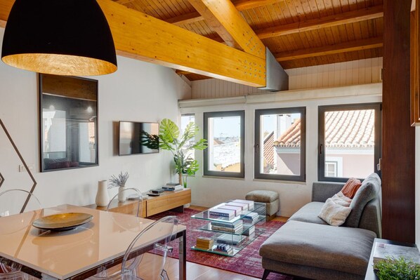 A modern living room with a wooden ceiling, a sofa, a coffee table, and a dining area with a glass table and chairs.