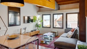Un salon moderne avec un plafond en bois, un canapé, une table basse et un coin repas comprenant une table et des chaises en verre.