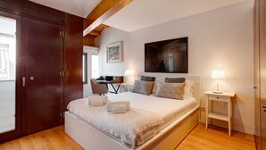 Une chambre avec un grand lit, des poutres apparentes en bois au plafond, un bureau et une chaise.