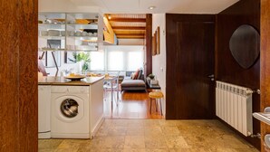 A compact kitchen with a washing machine, a dining area with a table and chairs, and a living space with a sofa. - Amazing Tailor Made Penthouse (Lisboa)