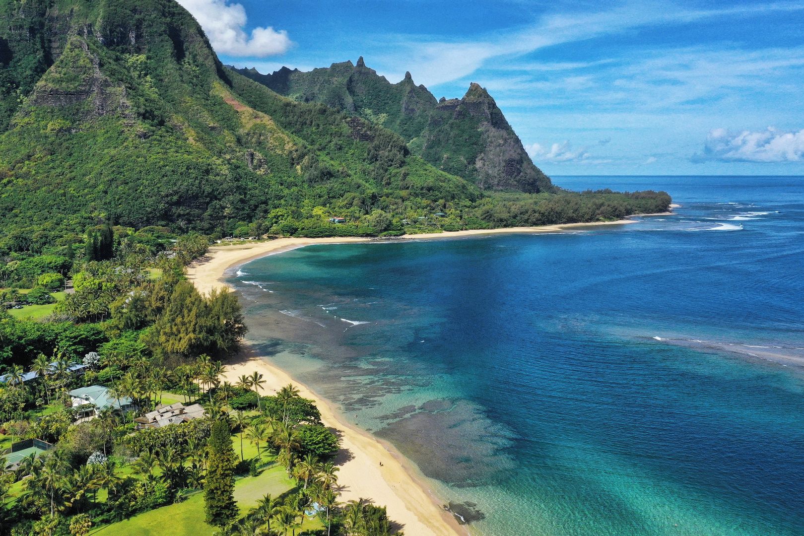 Un paysage côtier avec une plage, des eaux d’un bleu limpide et des collines verdoyantes.